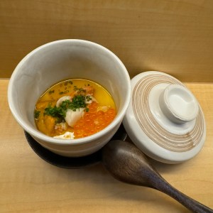 Egg custard and rose in a ceramic cup with a wooden spoon and lid.