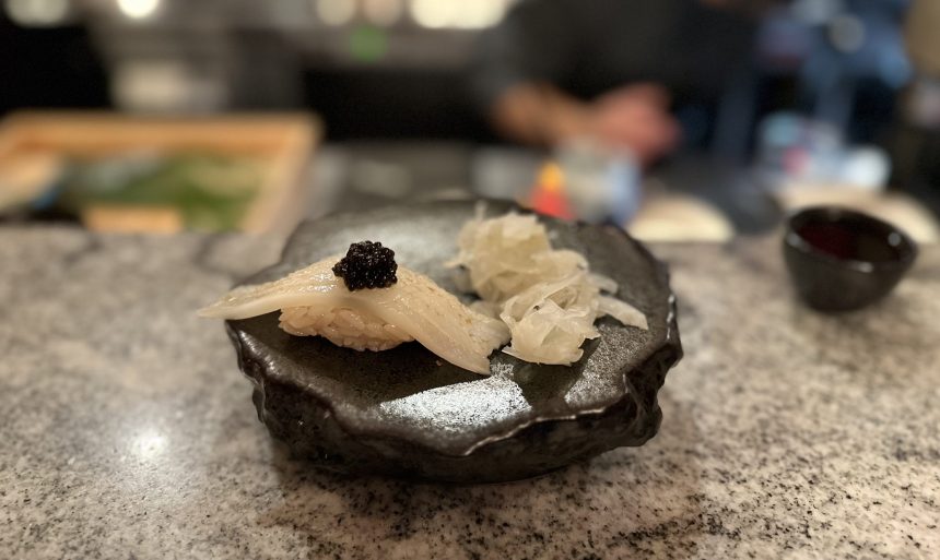 Squid and caviar kaiseki sushi nigiri on a black plate with sliced pickled ginger