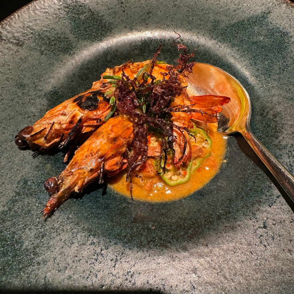 Chargrilled tiger prawns on an orange sauce in a charcoal coloured bowl with a spoon