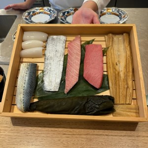 Assorted raw fish in a wooden crate at Tsuzumi Omakase.